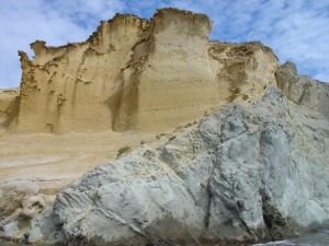 En primer plano las rocas volcnicas riodacitas. Al fondo el acantilado en las areniscas marinas del Plioceno con desarrollo de cornisas por la meteorizacin